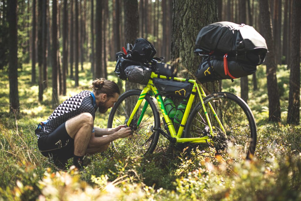 Coaching cycliste.
Entrainement cycliste - Se préparer pour une longue distance.
Cycliste accroupie regardant son vélo posé contre un arbre dans une forêt.
Le vélo est chargé de nombreuses sacoches de bikepacking sur le guidon, dans le cadre et sur la selle.