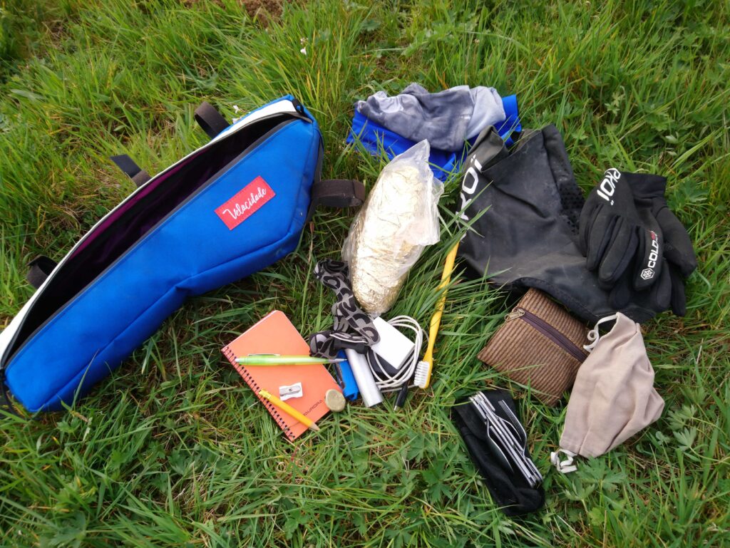Bikepacking en image.
Photo de la sacoche de cadre avec les affaires étalées à coté sur la pelouse.